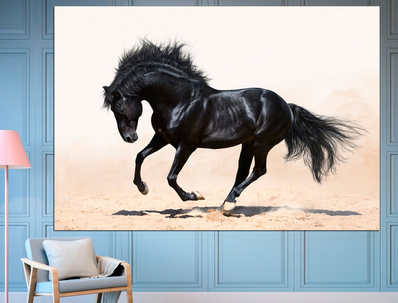 May include: A black horse runs across a sandy area with its mane and tail flowing in the wind. The horse is in mid-stride with its front legs extended and its back legs tucked under its body. The background is a white sky with some clouds.