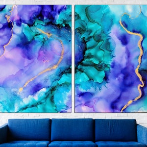 May include: Two-panel abstract art print featuring a blend of blues, teals, and purples with gold accents. The artwork has a fluid, watercolor-like appearance, with a dark blue sofa in the foreground and a white brick wall in the background.
