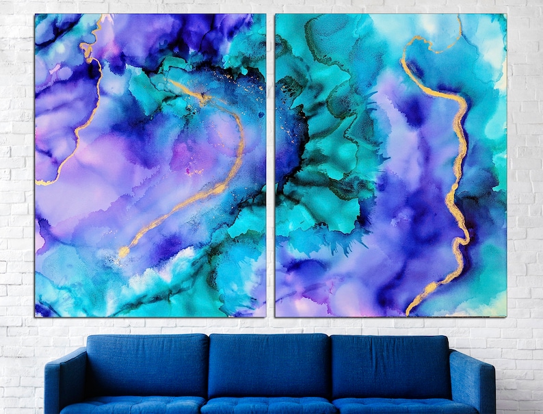 May include: Two-panel abstract art print featuring a blend of blues, teals, and purples with gold accents. The artwork has a fluid, watercolor-like appearance, with a dark blue sofa in the foreground and a white brick wall in the background.