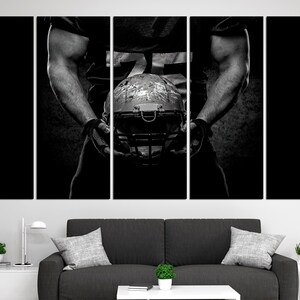 May include: A black and white photo of a football player holding a football helmet. The player is wearing a jersey and has a determined expression on their face.