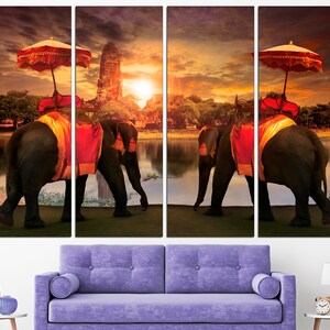 May include: Two elephants adorned with colorful fabric and parasols walk along a riverbank at sunset. The elephants are in front of a temple with a golden spire. The scene is a vibrant depiction of Thai culture.