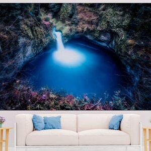 May include: A blue waterfall cascades into a deep, dark pool surrounded by lush green foliage. The water is illuminated by the sunlight, creating a bright, ethereal glow.