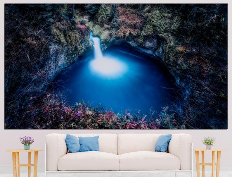 May include: A blue waterfall cascades into a deep, dark pool surrounded by lush green foliage. The water is illuminated by the sunlight, creating a bright, ethereal glow.