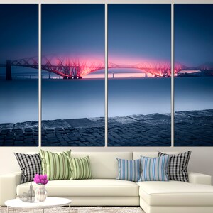 May include: A panoramic view of a bridge illuminated in pink and orange at dusk. The bridge spans a body of water with a stone pier in the foreground. The sky is a deep blue with a hint of purple.