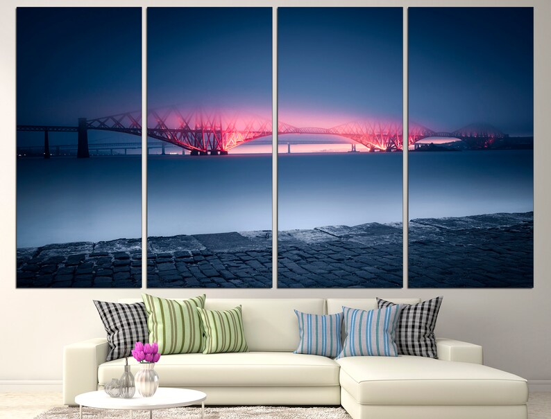 May include: A panoramic view of a bridge illuminated in pink and orange at dusk. The bridge spans a body of water with a stone pier in the foreground. The sky is a deep blue with a hint of purple.
