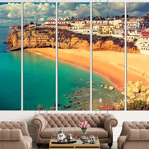 May include: A panoramic view of a coastal town with white buildings perched on a cliff overlooking a turquoise ocean and a sandy beach.