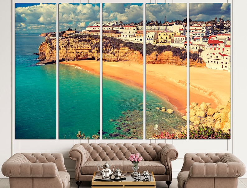 May include: A panoramic view of a coastal town with white buildings perched on a cliff overlooking a turquoise ocean and a sandy beach.