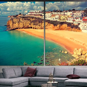 May include: A panoramic view of a coastal town with white buildings perched on a cliff overlooking a sandy beach and turquoise water.