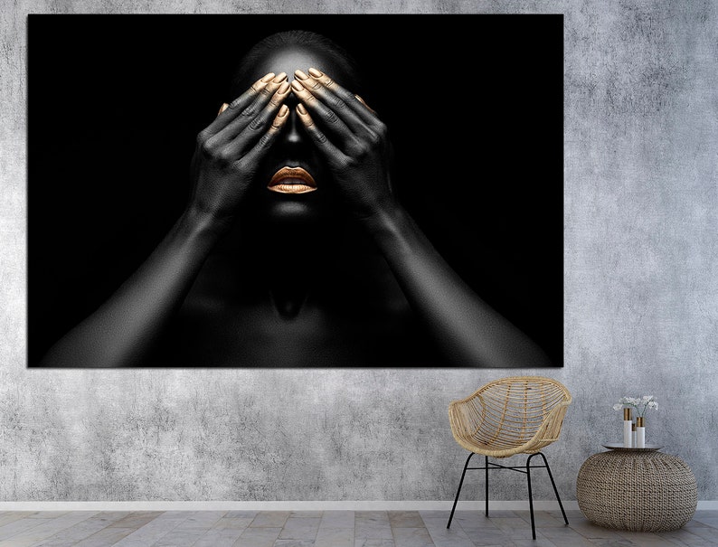 May include: A person with black skin and gold painted lips and fingernails covers their eyes with their hands. The background is black.