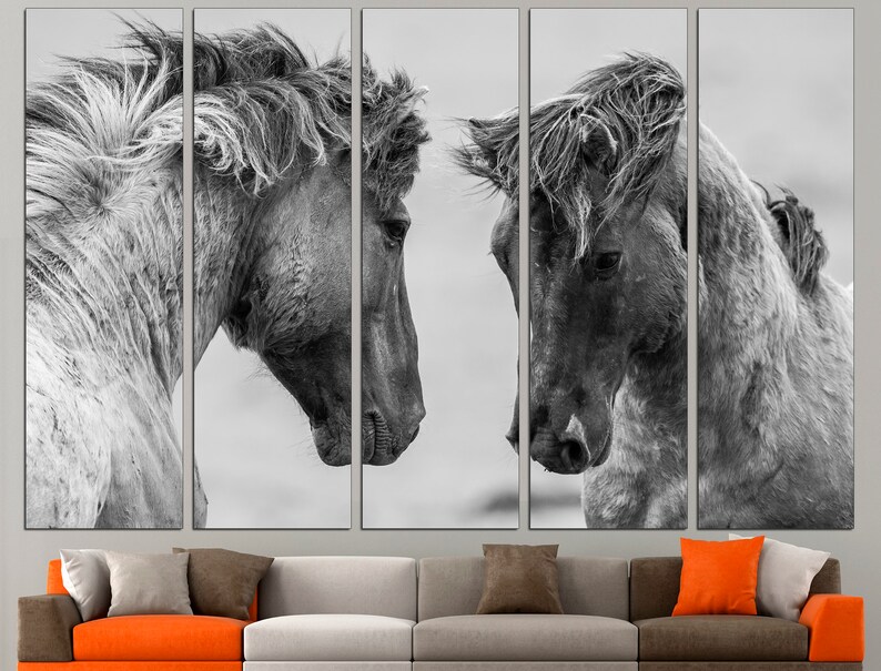 May include: A black and white photograph of two horses' heads facing each other. The horses' manes are flowing in the wind. The background is a blurred out grey.