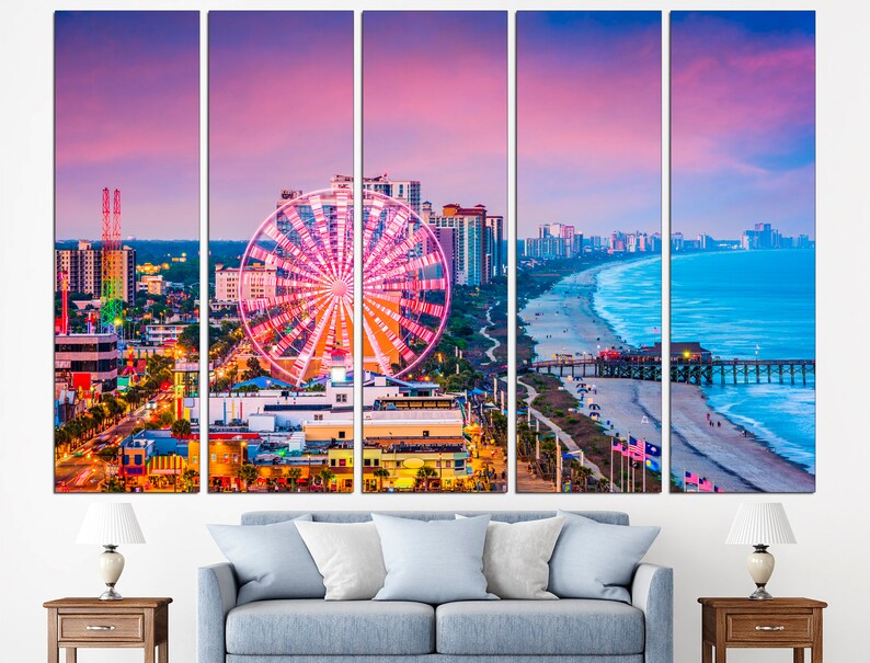 May include: A panoramic view of Myrtle Beach, South Carolina at sunset. The image features a Ferris wheel, a pier, a beach, and the city skyline. The sky is a vibrant pink and orange, and the water is a deep blue.