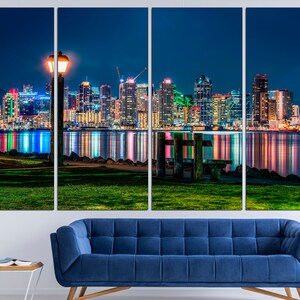 Puede incluir: Una ciudad nocturna con una vista de un horizonte urbano reflejado en el agua. La ciudad est&aacute; iluminada con luces de colores. Una farola est&aacute; en primer plano.