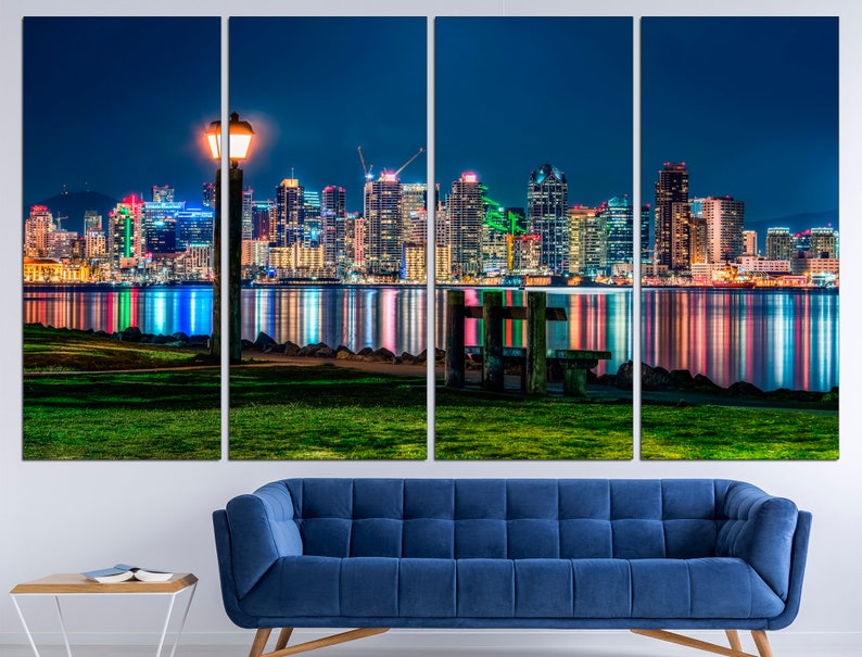Puede incluir: Una ciudad nocturna con una vista de un horizonte urbano reflejado en el agua. La ciudad est&aacute; iluminada con luces de colores. Una farola est&aacute; en primer plano.