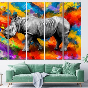 May include: A multi-panel canvas print featuring a white rhinoceros with a colorful paint splatter background. The rhinoceros is depicted in a realistic style, with a detailed texture and a prominent horn. The background is a vibrant mix of colors, including red, orange, yellow, blue, green, and purple.