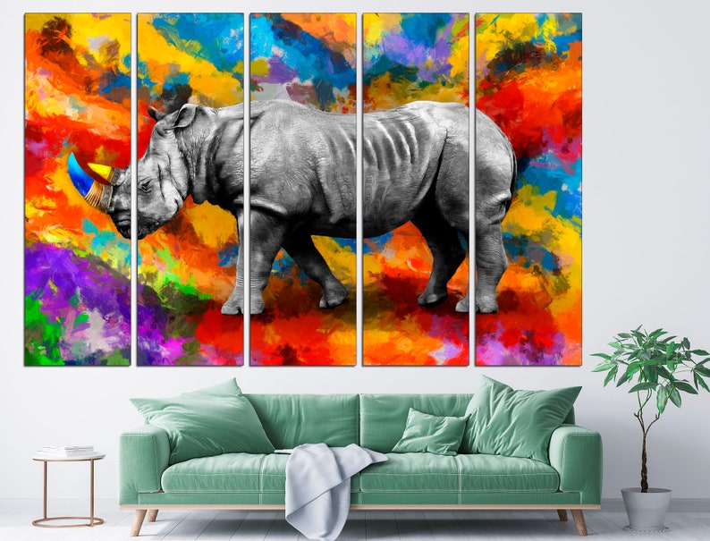 May include: A multi-panel canvas print featuring a white rhinoceros with a colorful paint splatter background. The rhinoceros is depicted in a realistic style, with a detailed texture and a prominent horn. The background is a vibrant mix of colors, including red, orange, yellow, blue, green, and purple.