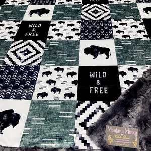 May include: A black and white patterned blanket with a buffalo plaid design and the words "Wild & Free" repeated throughout. The blanket is made of a soft, plush material and has a gray minky backing.