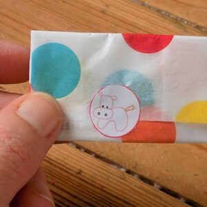 Puede incluir: Un sobre de papel blanco con lunares de colores y una pegatina de un hipop&oacute;tamo rosa. El sobre est&aacute; doblado por la mitad y tiene un patr&oacute;n de lunares rojos, naranjas, azules y amarillos.