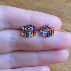 Puede incluir: Un par de pendientes de bot&oacute;n con un dise&ntilde;o de cubo de Rubik colorido. Los pendientes est&aacute;n hechos de pl&aacute;stico transparente con un dise&ntilde;o impreso.