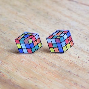 May include: A pair of colorful, transparent cube earrings. Each earring is a 3D representation of a Rubik's Cube with a variety of colors, including red, blue, yellow, green, and orange.