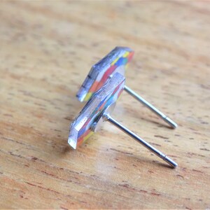 Puede incluir: Un par de pendientes de bot&oacute;n geom&eacute;tricos coloridos con postes de plata. Los pendientes est&aacute;n hechos de resina y tienen un dise&ntilde;o multicolor.