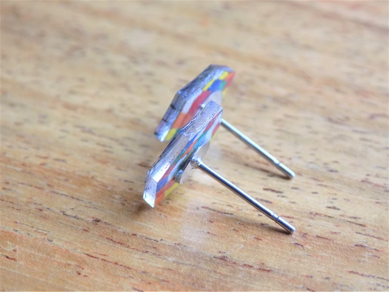 Puede incluir: Un par de pendientes de bot&oacute;n geom&eacute;tricos coloridos con postes de plata. Los pendientes est&aacute;n hechos de resina y tienen un dise&ntilde;o multicolor.