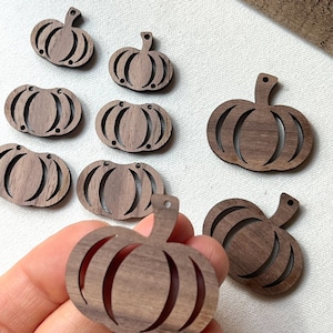 May include: A collection of wooden pumpkin cutouts. The pumpkins are a warm brown color with a carved design. Each pumpkin has a stem and a small hole at the top for hanging. The pumpkins are ideal for fall crafts and decorations.