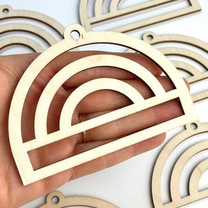 May include: Several unfinished wooden rainbow-shaped ornaments. Each ornament features a layered design with a semi-circular top and a rectangular base. The ornaments have a small hole at the top for hanging.