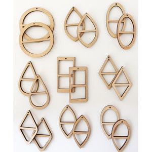 May include: A collection of unfinished wooden earrings in various geometric shapes, including circles, teardrops, rectangles, and diamonds. Each pair has a horizontal bar across the center and a small hole at the top for hanging.