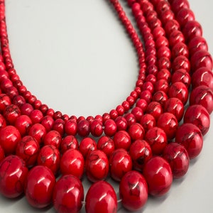 May include: Close-up of several strands of red gemstone beads. The beads vary in size, from small to large, and have a marbled appearance. The beads are strung together, creating a necklace or bracelet design.
