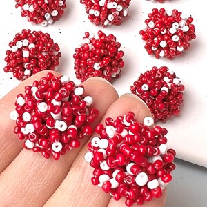 May include: A collection of red and white beaded clusters. The beads are small and tightly packed, creating a textured, spherical shape. The color combination is striking, with the red beads dominating and the white beads interspersed throughout.