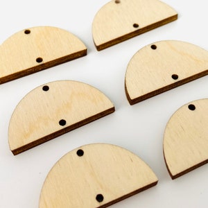 May include: Several unfinished wooden half-circle shapes with two small holes and a single hole for hanging. The wood has a light, natural color with darker edges. These craft supplies are ideal for DIY projects.