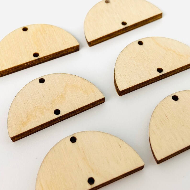 May include: Several unfinished wooden half-circle shapes with two small holes and a single hole for hanging. The wood has a light, natural color with darker edges. These craft supplies are ideal for DIY projects.