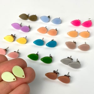 May include: A collection of colorful teardrop-shaped stud earrings in various shades, including pink, yellow, green, and blue. The earrings have silver posts and are displayed on a white surface. The earrings are a fashion accessory.