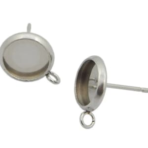 May include: Two silver-colored earring posts with a round, recessed setting and a small loop at the bottom. The posts are designed to hold a stone or other decorative element. The earrings are shown against a white background.