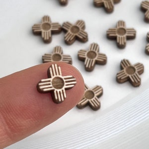 May include: Close-up of several small, wooden, cross-shaped embellishments. Each embellishment features a central circle with four arms, each with three parallel lines. The embellishments are a light brown color.