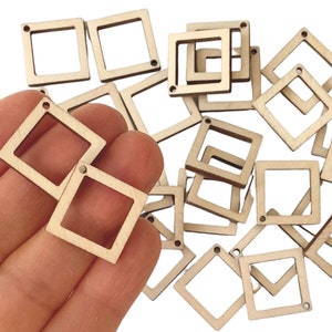 May include: A collection of small, square wooden frames with a square cut-out in the center. Each frame has a small hole in one corner. The frames are a light, natural wood color and are scattered across a white surface.