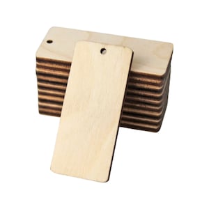 May include: A stack of rectangular wooden tags with a hole at the top for stringing. The tags are a light, natural wood color, with visible grain. One tag is separated from the stack, showing the front and side view of the tag.