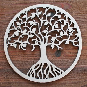 May include: A circular, light-colored wooden cutout of a tree with roots, a trunk, branches, and leaves. The tree is enclosed within a circular frame. The background is a dark brown wooden surface.