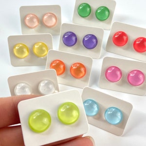May include: A collection of colorful stud earrings in various shades, including pink, green, purple, red, yellow, orange, clear, and blue. Each pair is displayed on a white card, showcasing the round, glossy design.