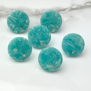 May include: Six round, turquoise-colored beads with a marbled white pattern. Each bead has a small hole in the center. The beads are arranged on a white surface.