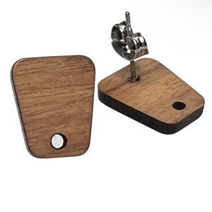 May include: Two wooden stud earrings with a rectangular shape and rounded top. The earrings are a medium brown color with a visible wood grain. Each earring has a silver-colored post and backing. One earring has a small, round magnet.