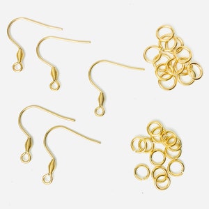 K&ouml;nnte beinhalten: Eine Sammlung goldfarbener Ohrhaken und Biegeringe. Die Ohrhaken haben ein gebogenes Design mit einem spiralf&ouml;rmigen Federdetail. Die Biegeringe sind klein, kreisf&ouml;rmig und ebenfalls goldfarben. Diese Komponenten werden f&uuml;r die Schmuckherstellung verwendet.