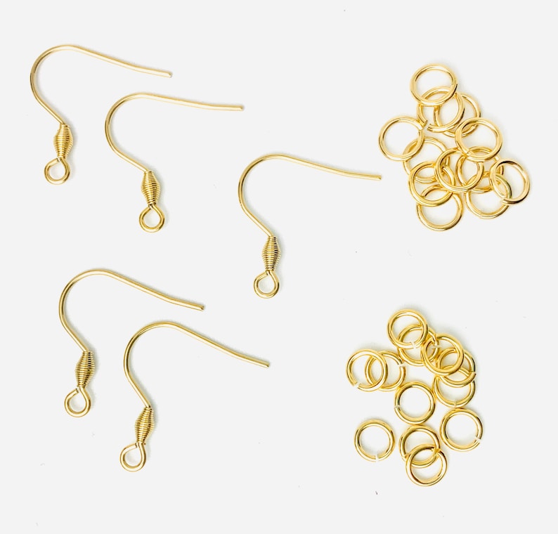 K&ouml;nnte beinhalten: Eine Sammlung goldfarbener Ohrhaken und Biegeringe. Die Ohrhaken haben ein gebogenes Design mit einem spiralf&ouml;rmigen Federdetail. Die Biegeringe sind klein, kreisf&ouml;rmig und ebenfalls goldfarben. Diese Komponenten werden f&uuml;r die Schmuckherstellung verwendet.