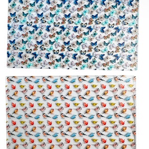 May include: Two rectangular glass cutting boards. The top board features a dense pattern of blue, teal, and white butterflies. The bottom board displays a repeating pattern of small birds in red, yellow, and blue colors against a white background.