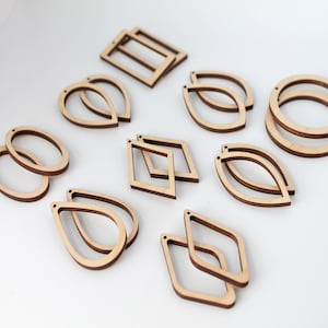 May include: A collection of unfinished wooden earring components in various geometric shapes, including teardrops, ovals, and rectangles. The components are light brown with a natural wood grain, and are designed for crafting earrings. The shapes vary in size.