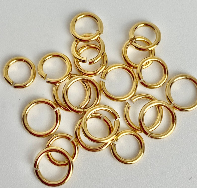 K&ouml;nnte beinhalten: Eine Ansammlung kleiner, goldfarbener Binderinge, teils offen, teils geschlossen, auf wei&szlig;em Untergrund. Die kreisf&ouml;rmigen Ringe sind vermutlich aus Metall und werden f&uuml;r Schmuckherstellung oder Bastelarbeiten verwendet.