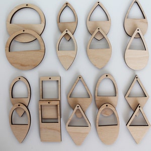 May include: A collection of unfinished wooden earring blanks in various shapes, including circles, teardrops, and squares. Each blank has a small hole for hanging and a cutout design. The natural wood grain is visible.