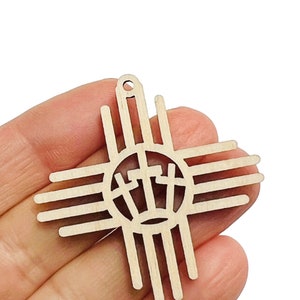 May include: A wooden cross pendant featuring a sun symbol design with three crosses inside a circle. The pendant is light brown and has a small hole at the top for hanging. The design is cut out of the wood.