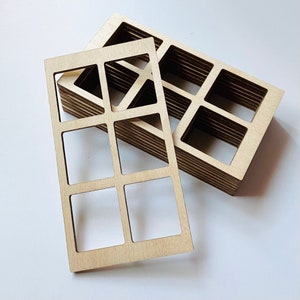 May include: Several unfinished wooden rectangular frames with square cutouts. One frame is in front of a stack of similar frames. The frames are made of light-colored wood and have a natural finish. The design is geometric and modern.