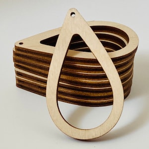 May include: A stack of unfinished wooden teardrop-shaped earring blanks. Each blank has a hole at the top for attaching earring hooks. The wood has a natural, light brown color with visible grain.